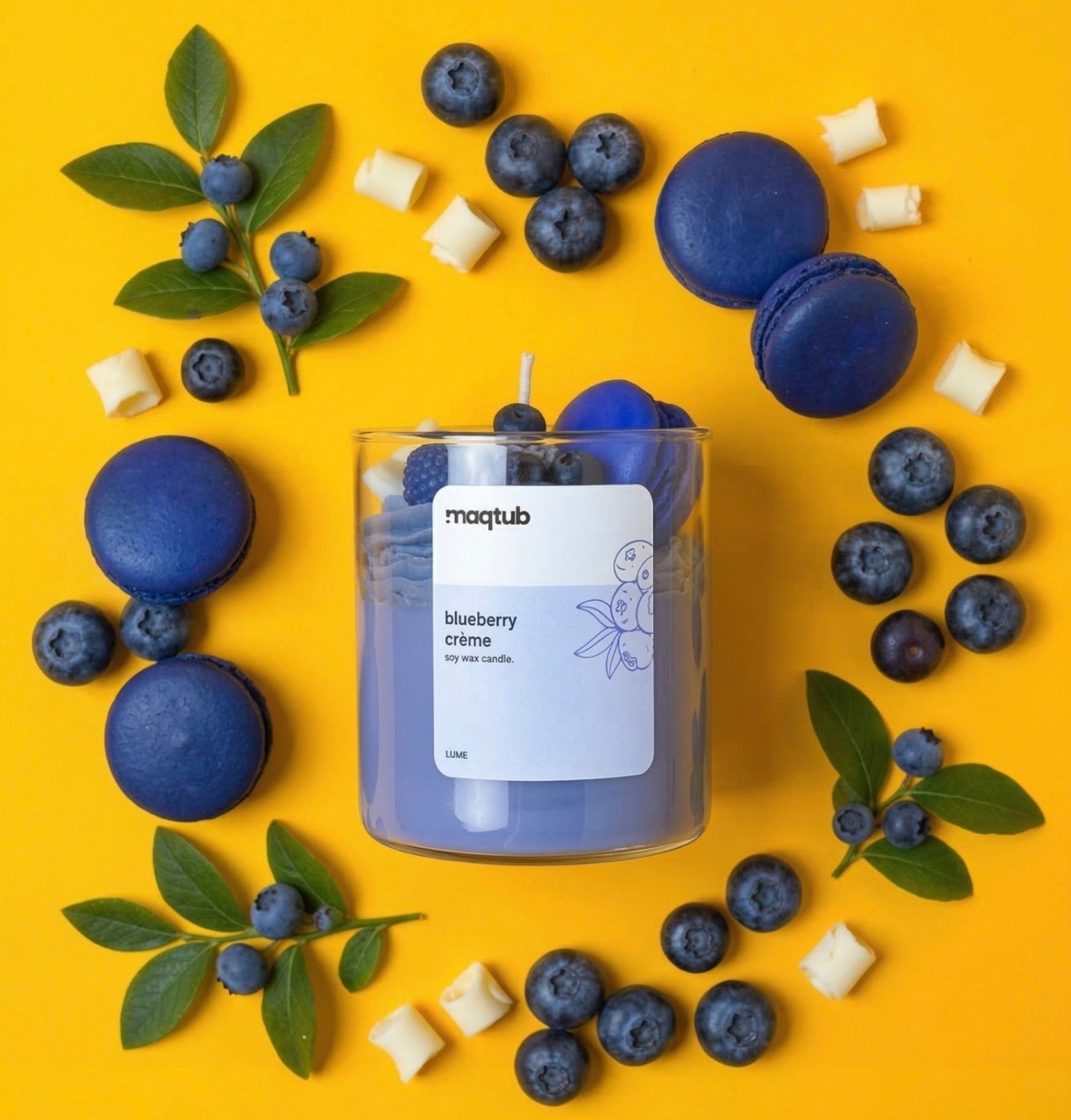 Blueberry Scented Candle labeled surrounded by blueberries and macarons on a yellow background